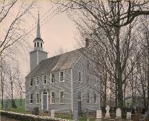 Corner view of Covenanters' Church, showing the evenly spaced multi-paned sash windows, and its setting on treed site surrounded by a burial ground, 1993.; Parks Canada Agency/ Agence Parcs Canada, 1993