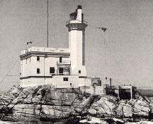 Vue générale du phare de l'île Triple, qui montre les lignes sobres et les fins ornements, y compris les consoles décoratives qui soutiennent la plate-forme surmontée d’une lanterne en fer.; Parks Canada Agency / Agence Parcs Canada.