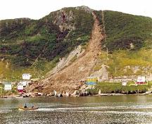 Picture showing the destruction caused by the landslide of August 1973. The remains of houses destroyed by the landslide can be seen at the water's edge.; Government of Newfoundland and Labrador 1973/ HFNL 2009