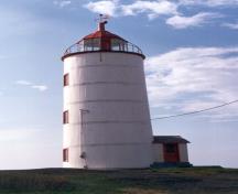 Side view of the Lighttower, showing its short, circular, slightly tapered masonry, and the vertical white wood boards, girded by five metal hoops, 1989.; Ministère des Affaires culturelles du Quebec / Quebec Ministry of Cultural Affairs, 1989.