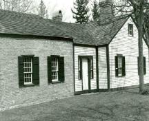 Vue de la façade latérale du logement de l'officier subalterne de l'intendance, qui montre les fenêtres à carreaux multiples, munies de volets, vers 1989.; Parks Canada Agency / Agence Parcs Canada, ca./vers 1989.