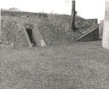View of the east Powder Magazine, showing the low, partially subterranean, inconspicuous massing of the reinforced, rectangular, brick structures, 1989.; Parks Canada Agency / Agence Parcs Canada, 1989.