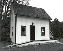 Corner view of the Storehouse, Lock Office, showing the gable roof and board-and-batten wood siding, 1989.; Public Works and Government Services Canada / Travaux publics et Services gouvernementaux Canada, 1989.