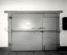 View of the interior of the Barrack, showing the metal door and door hardware, 1990.; Parks Canada Agency / Agence Parcs Canada, 1990.