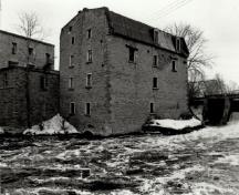 View of the West Mill, showing the exterior walls of stone, 1972.; Agence Parcs Canada / Parks Canada Agency, 1972.