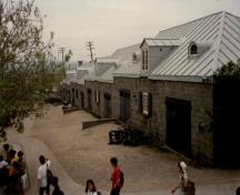 View of the Cannon Carriage Store, showing the hipped roof of sheet metal with batten seams, and the semicircular dormers above the doors, 1991.; Agence Parcs Canada / Parks Canada Agency, 1991.