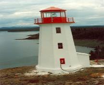 Façade latérale du Phare de la station de phare, qui montre sa lanterne octogonale coiffée d’un toit à faible pente, île Battle, 1990.; Canadian Coast Guard / Garde côtière canadienne, 1990.
