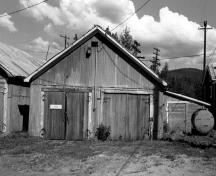Façade of the Garage and Storage Building, showing the building’s simple, rectangular form, gable roofs and large double doors, 1988.; Parks Canada Agency / Agence Parcs Canada, 1988.