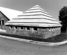 Vue en angle du Bâtiment 7, montrant la toiture en chape de béton recouverte de pierres lisses posées de façon à créer des bandes horizontales, 1980.; National Defense Ministry of Canada / Ministère de la Défense Nationale (1980).