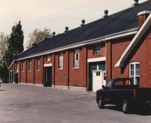 View of the exterior of RMC Building 3, showing the long, symmetrical, single-volume, pitched roof shed, 1993.; Parks Canada Agency / Agence Parcs Canada, 1993.