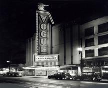 Vue générale du Théâtre Vogue, qui montre la haute tour à enseignes lumineuses qui domine la façade, encadrée de néons et surmontée d'une silhouette stylisée de la déesse Diane.; Vancouver Public Library, Historical Photo Collection, 33461.