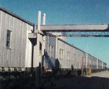 Vue générale du train modulaire B, montrant le revêtement extérieur en métal et la taille, la forme et la disposition des portes et des fenêtres, qui sont régies par la fonction de chaque module, 1998.; Canada, North Warning System Office / Bureau du système d'alerte du Nord, 1998.