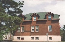 Side facade of the Arc Biotech Building (No.34); showing the subtle brick coursing pattern on the red brick walls, painted wood trim and the high concrete foundation, 1999.; Agence Parcs Canada / Parks Canada Agency, 1999.