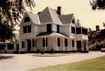 View of the main façade of Heritage House (Building 54), showing the large scale and massing of the house, which consists of a two-and-a-half storey structure with a verandah around two sides and a hip and gable roof, 1982.; Agence Parcs Canada / Parks Canada Agency, Janet Wright and Monique Trepanier, 1982.