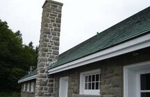 View of the exterior of the Bathhouse, showing the exterior materials and finishes, particularly the rough-cut, irregularly coursed stone, wood trim, and cedar roof shingles.; Parks Canada Agency / Agence Parcs Canada.