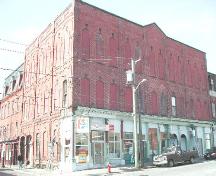 This photograph shows the contextual view of the building and the Roman arch windows on the top floor, the segmented arch windows on the second floor and three Roman archways at the storefront. ; City of Saint John