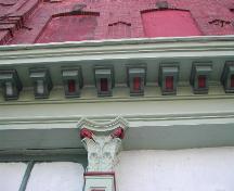 This photograph shows a portion of the overhanging storefront cornice, dentils, and the top of one of the columns.; City of Saint John 2004