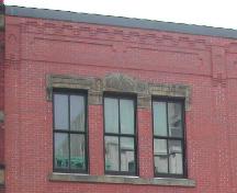 This photograph shows the sets of triple windows with decorative headers and the roofline cornice, 2004; City of Saint John