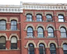 This photograph shows the segmented arch windows and the decorative cornice.  The column that runs vertically through the centre of the building and the sandstone ledge that runs horizontally along the returns of each window arch, 2004; City of Saint John