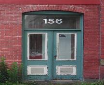 This image provides a view of the paired wood doors with glass panels below a segmented arched opening framing a rectangular transom window, 2005.; City of Saint John