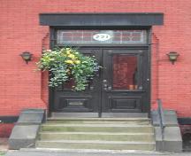 This image provides a view of the entry with a sandstone lintel over a rectangular, stained glass transom window and paired wood doors with glass panels in the upper half, 2005.; City of Saint John