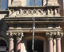 Cette photographie montre le grand entablement au dessus de l'entrée et illustre les chapiteaux ornés avec les motifs des plantes et des animaux, 2005.; City of Saint John
