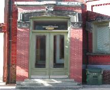 This photograph shows the entrance of the building, and the elaborate sandstone entablature above the transom window and paired wooden doors, 2005.; City of Saint John