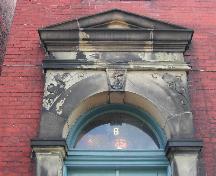 This photograph shows the pediment entablature and transom window above the entrance and the anchor insignia in the keystone, 2005.; City of Saint John
