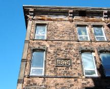 This photograph shows the large metal cornice and the 1879 datestone (2005); City of Saint John
