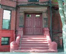 This photograph shows the full view of one of the two main symmetrical entrances, and illustrates the broad entablature supported by Ionic columns, 2005; City of Saint John