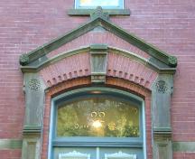 This photograph shows the entablature over the entrance, and illustrates the sandstone keystone, and segmented arch transom window, 2005; City of Saint John