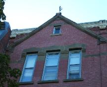 This photograph shows one of the flush gables that extend above the roof-line cornice, and illustrates the sandstone tracery that connects the lintels of the windows, 2005; City of Saint John