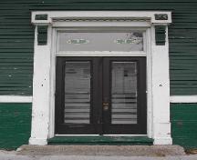 This image provides a view of one of the Orange Street entries including an entablature with brackets, dentils and pilasters, a transom window and paired wood doors with glass panels, 2005; City of Saint John