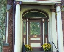 This photograph shows the entranceway, and illustrates the columns with ionic capitals, segmented arch transom window, sidelights, and wide wooden door, 2005; City of Saint John