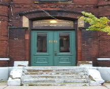 This image provides a view of the entrance consisting of a segmented arch brick and sandstone hood mold, a pronounced keystone, a segmented arched transom window and paired wood doors with glass panels, 2005
; City of Saint John