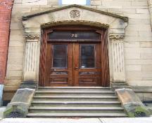 Cette image montre l'entrée comprenant un fronton de pierre, des pilastres cannelés avec chapiteaux corinthiens, un imposte et des portes doubles en bois avec panneaux de verre, 2005; City of Saint John