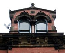 This image provides a view of the gable dormer crowned with a finial, encasing Roman arched windows above the bracketed cornice, 2005; City of Saint John
