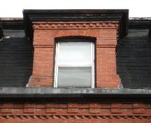 Cette image montre la lucarne centrale à arche segmentée ornée de dentelets au-dessus de la corniche, 2005; City of Saint John