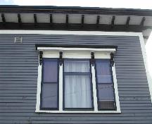 This photograph shows the roof-line cornice with modillions, and one of the triple windows under a bracketed entablature, 2005; City of Saint John
