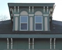 This image provides a view of the central dormer with a hipped roof encasing two Roman arched openings above wide eaves supported by a series of paired, scrolled brackets, 2006
; City of Saint John