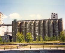 View of the exterior of the Annex, showing the massing, which consists of ten, tall concrete cylinders, inter-linked so as to form a continuous wall and a glazed storey which sits atop the complex of silos, 1995.; Parks Canada Agency / Agence Parcs Canada, J. Hallé, 1995.