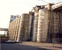 Vue des cylindres de l'annexe, qui montre les ouvertures dans la paroi extérieure de béton, dans la partie inférieure, qui permettent d’accéder aux parties mécaniques situées sous les silos, 1995.; Parks Canada Agency / Agence Parcs Canada, J. Hallé, 1995.