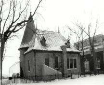 View of the Administration Building, showing the stone structure with a steep bell-cast roof, decorative dormers and an angled, round entrance tower with a steep  conical roof, 1992.; Agence Parcs Canada / Parks Canada Agency, 1992.