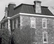 Corner view of the Office Building, showing the sandstone exterior walls laid in random courses and the mansard roof with chimneys, 1985.; Parks Canada Agency / Agence Parcs Canada, 1985.