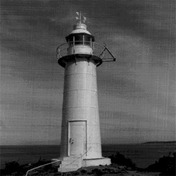 General view of the lighttower at King's Cove Head, showing the simple massing of the tower which consists of a smooth tubular form composed of a base, shaft, lantern platform and lantern with a lantern cap and prominent weathervane, 1989.; Canadian Coast Guard/Garde côtière canadienne, 1989.